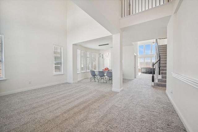 interior space featuring plenty of natural light, a towering ceiling, light colored carpet, and an inviting chandelier