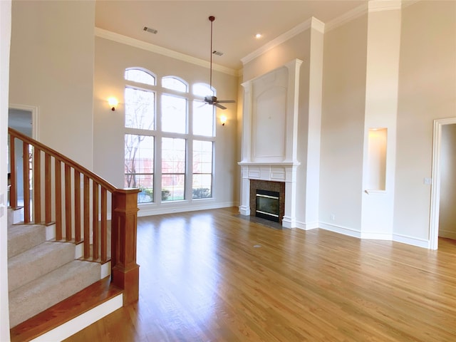 unfurnished living room featuring wood-type flooring, ornamental molding, ceiling fan, a fireplace, and a high ceiling