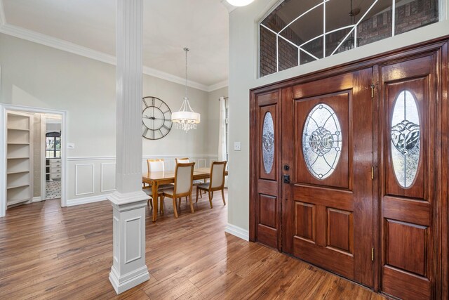 foyer entrance featuring wood-type flooring, ornate columns, crown molding, and a notable chandelier