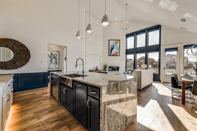 kitchen with light stone countertops, a kitchen island with sink, sink, pendant lighting, and an inviting chandelier