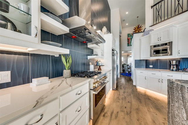 kitchen with white cabinets, light hardwood / wood-style flooring, decorative backsplash, light stone counters, and stainless steel appliances