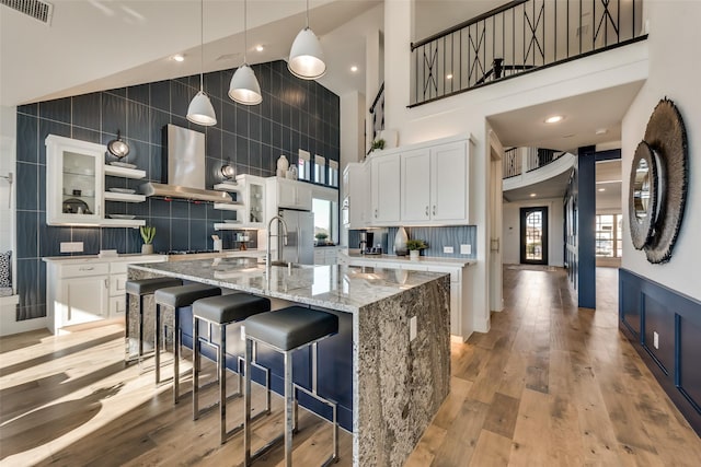 kitchen with island range hood, a center island with sink, white cabinets, and light wood-type flooring