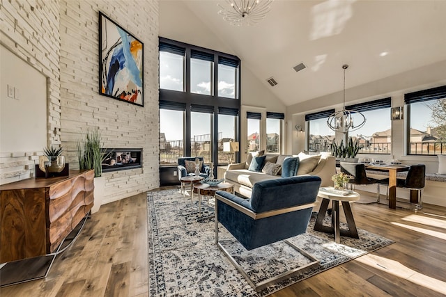 living room with hardwood / wood-style flooring, a fireplace, high vaulted ceiling, and an inviting chandelier