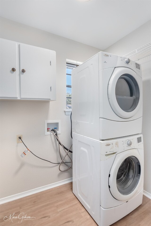 laundry room with cabinets, stacked washing maching and dryer, and light hardwood / wood-style flooring