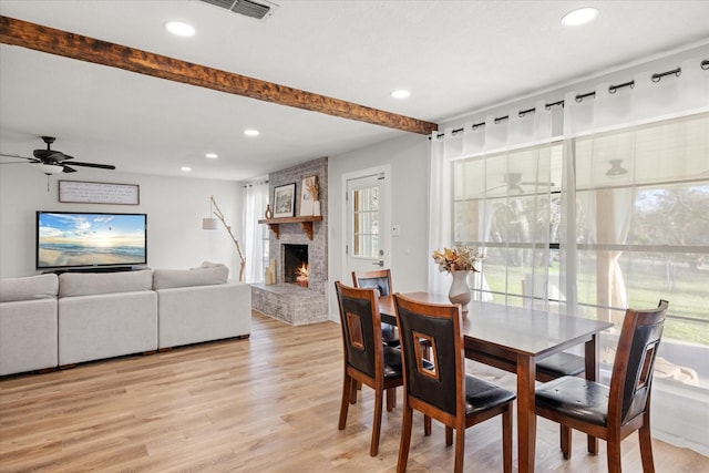 dining room with ceiling fan, a large fireplace, light wood-type flooring, and beam ceiling