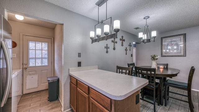 kitchen featuring pendant lighting, stainless steel refrigerator, a chandelier, washing machine and clothes dryer, and a textured ceiling