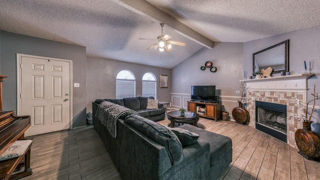 living room featuring ceiling fan, hardwood / wood-style floors, vaulted ceiling with beams, a fireplace, and a textured ceiling