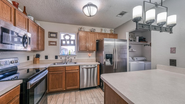 kitchen featuring appliances with stainless steel finishes, sink, hanging light fixtures, washer and clothes dryer, and a textured ceiling