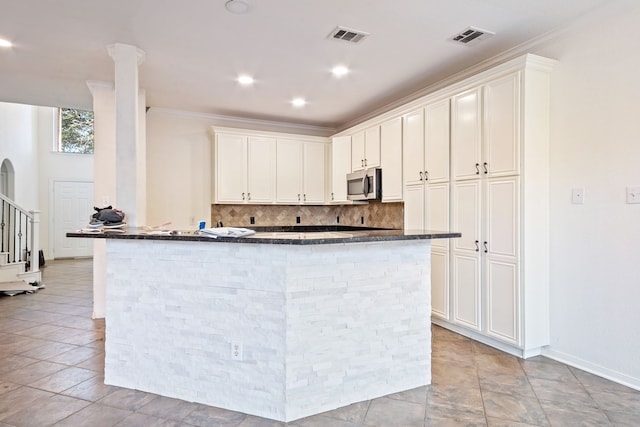 kitchen with tasteful backsplash, white cabinetry, dark stone counters, and ornamental molding