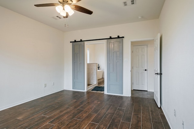 unfurnished bedroom featuring a barn door, ceiling fan, and ensuite bathroom