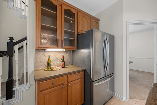 kitchen with tasteful backsplash, light tile patterned floors, stainless steel refrigerator, and dark stone countertops