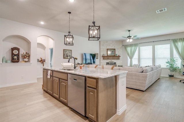 kitchen with ceiling fan, dishwasher, sink, a stone fireplace, and a kitchen island with sink