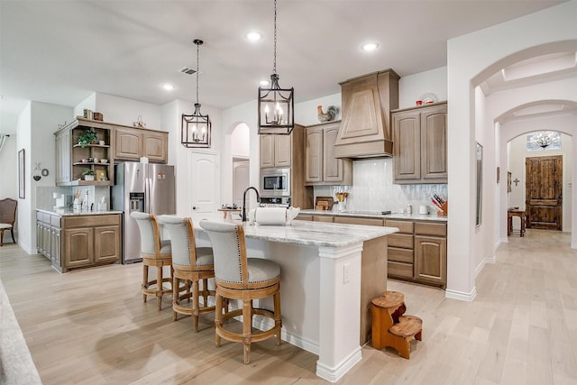 kitchen with custom exhaust hood, an island with sink, appliances with stainless steel finishes, and tasteful backsplash