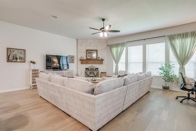 living room featuring light hardwood / wood-style floors, a stone fireplace, and ceiling fan