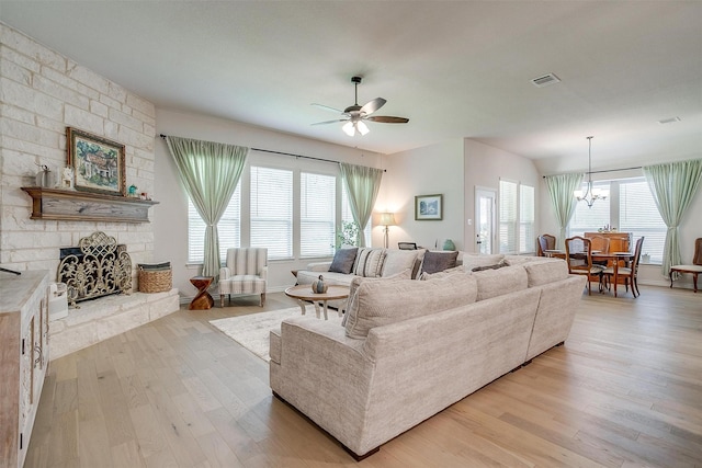 living room with a stone fireplace, light hardwood / wood-style flooring, and ceiling fan with notable chandelier