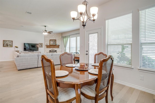 dining space featuring a stone fireplace, light hardwood / wood-style floors, and ceiling fan with notable chandelier