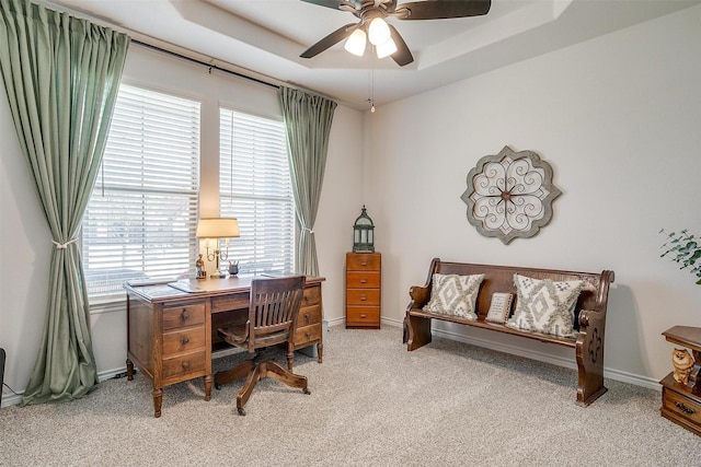 carpeted office featuring a tray ceiling and ceiling fan