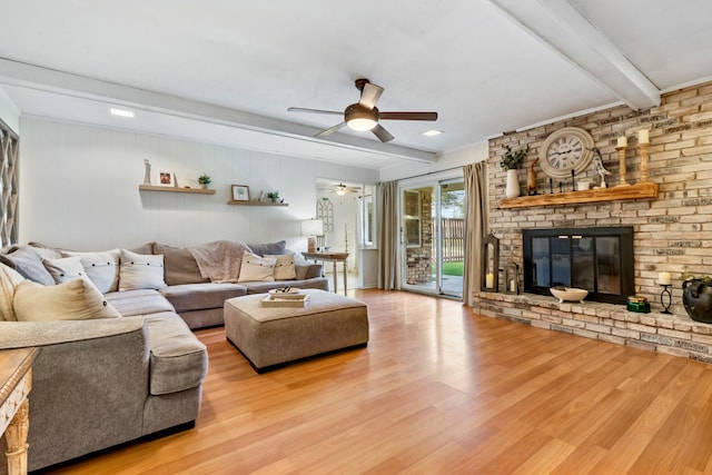 living room with beamed ceiling, light wood-type flooring, a fireplace, and ceiling fan