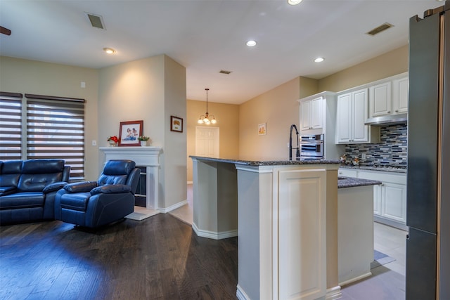 kitchen featuring white cabinetry, hardwood / wood-style flooring, a center island with sink, tasteful backsplash, and oven