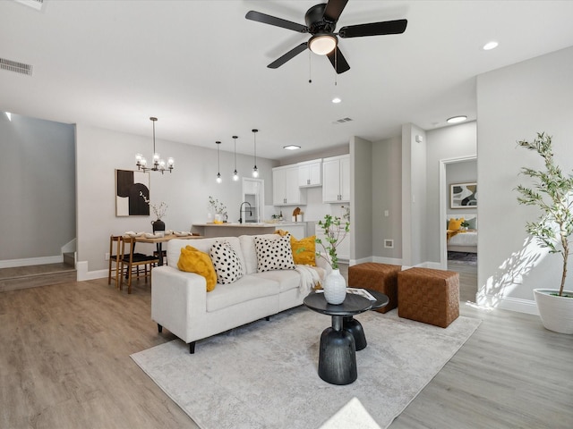 living room featuring ceiling fan with notable chandelier, light hardwood / wood-style flooring, and sink