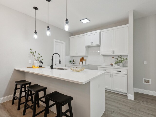 kitchen featuring tasteful backsplash, sink, decorative light fixtures, white cabinetry, and a breakfast bar area