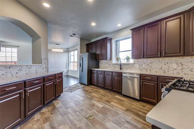 kitchen with sink, hardwood / wood-style flooring, appliances with stainless steel finishes, tasteful backsplash, and dark brown cabinetry