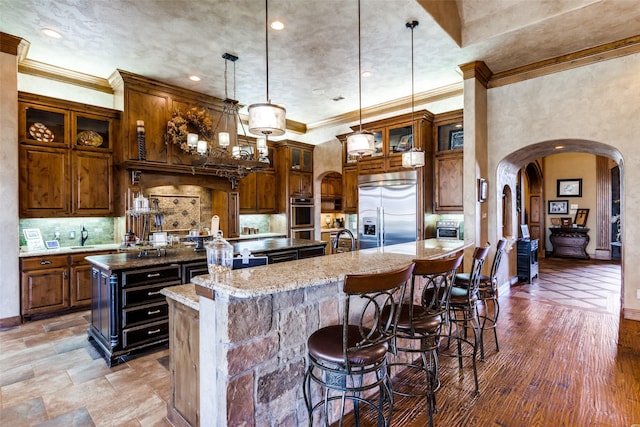 kitchen featuring appliances with stainless steel finishes, dark stone countertops, hanging light fixtures, backsplash, and an island with sink