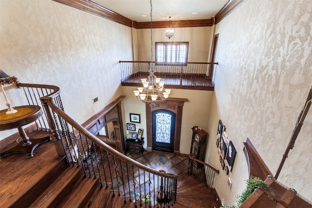 foyer featuring hardwood / wood-style flooring, ornamental molding, a towering ceiling, and an inviting chandelier