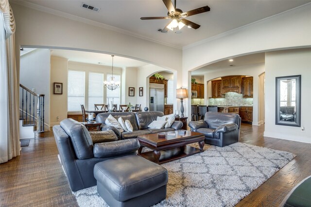 living room with dark wood-type flooring, ornamental molding, a healthy amount of sunlight, and ceiling fan with notable chandelier