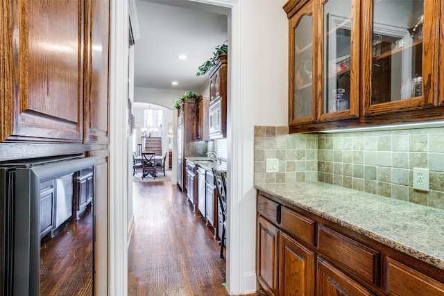 kitchen with light stone counters, ornamental molding, dark wood-type flooring, and tasteful backsplash