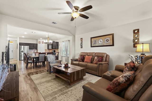 living room with ceiling fan with notable chandelier, lofted ceiling, and light hardwood / wood-style flooring