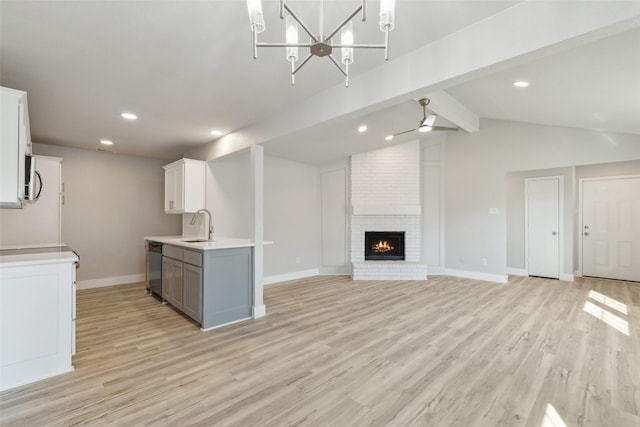 kitchen with stainless steel dishwasher, white cabinets, a fireplace, and light hardwood / wood-style flooring