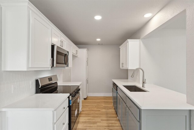 kitchen with sink, appliances with stainless steel finishes, white cabinetry, gray cabinetry, and light hardwood / wood-style floors