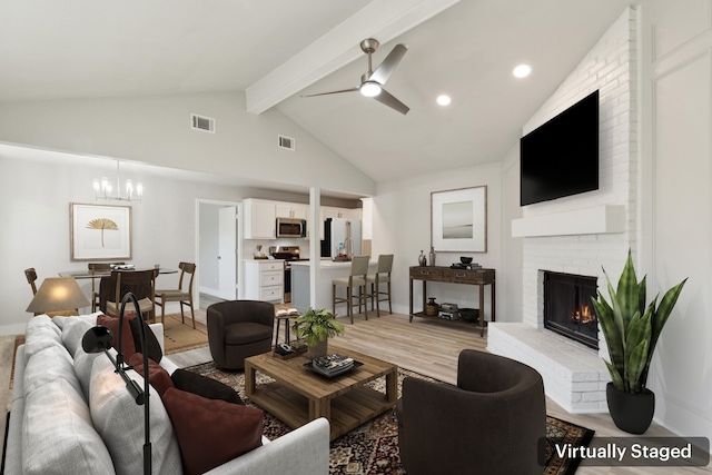 living room with beam ceiling, high vaulted ceiling, light hardwood / wood-style floors, a fireplace, and ceiling fan with notable chandelier