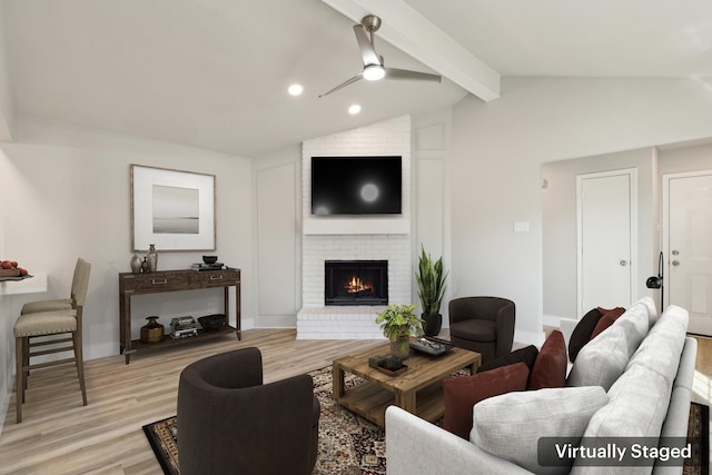 living room featuring vaulted ceiling with beams, ceiling fan, a brick fireplace, and light wood-type flooring