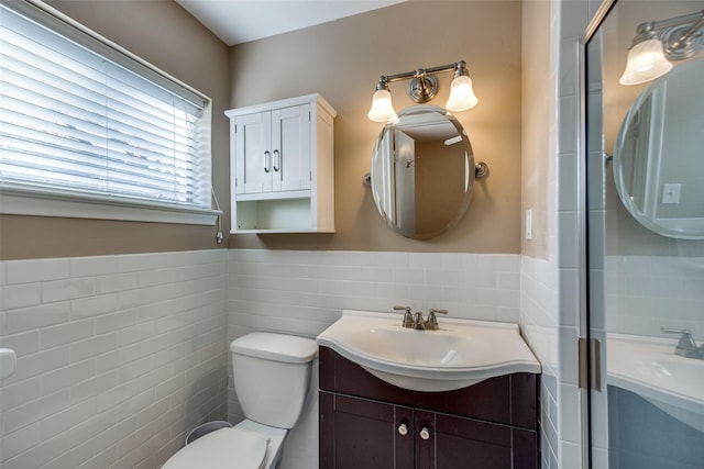 bathroom with vanity, a shower with shower door, toilet, and tile walls