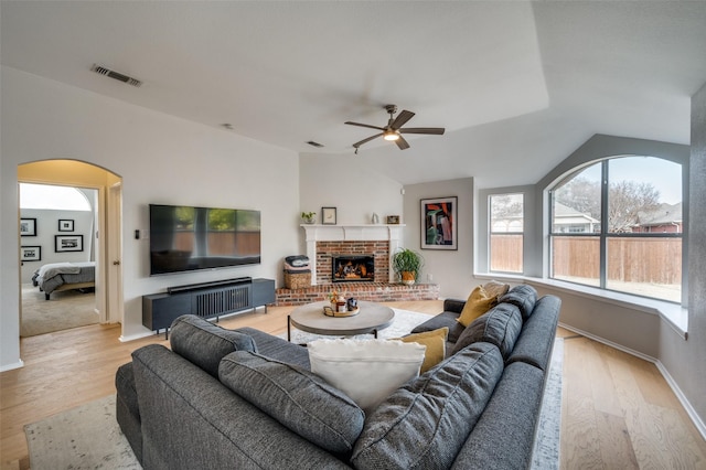 living room featuring ceiling fan, a brick fireplace, and light wood-type flooring