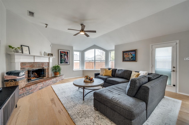 living room with ceiling fan, lofted ceiling, light wood-type flooring, and a brick fireplace