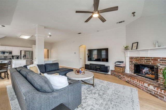 living room with a fireplace, light hardwood / wood-style flooring, ceiling fan, and vaulted ceiling