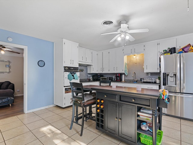 kitchen with light tile patterned floors, stainless steel fridge, tasteful backsplash, white cabinets, and oven