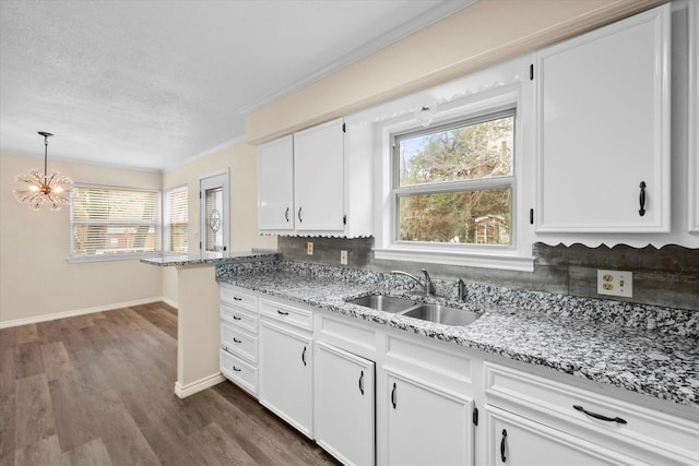 kitchen featuring sink, hanging light fixtures, light stone counters, a chandelier, and white cabinets