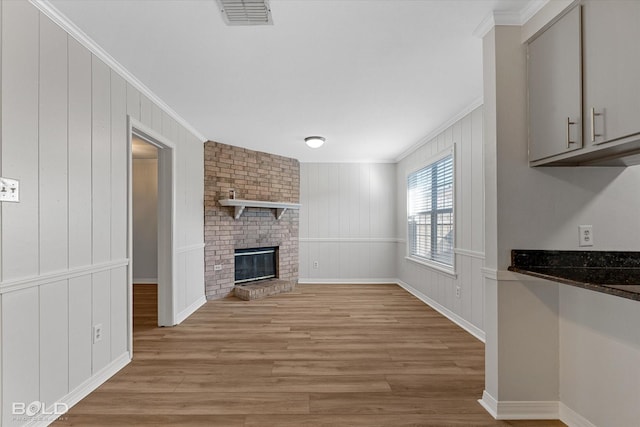 unfurnished living room with light wood-type flooring, ornamental molding, and a brick fireplace