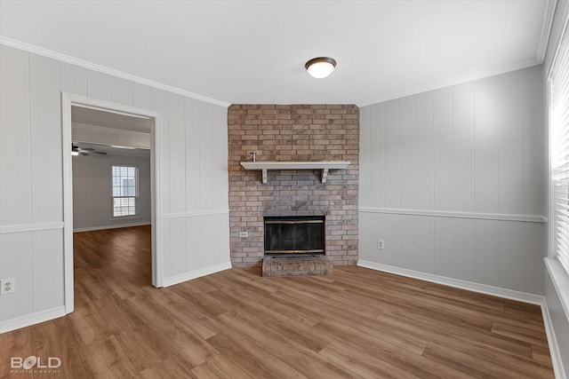 unfurnished living room featuring a fireplace, wood-type flooring, ceiling fan, and crown molding