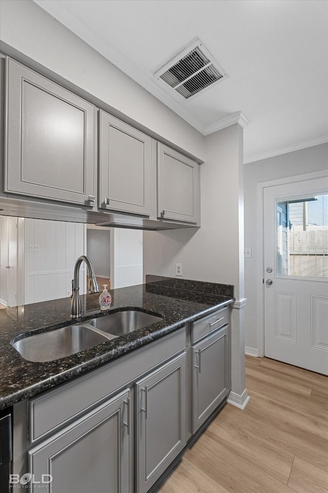 kitchen featuring dark stone countertops, light hardwood / wood-style flooring, ornamental molding, and sink