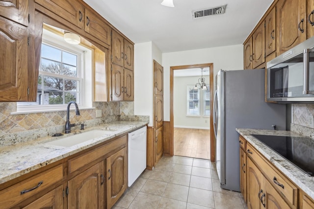 kitchen featuring white dishwasher, sink, decorative backsplash, light tile patterned floors, and light stone counters