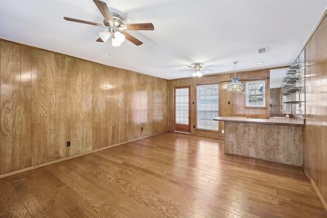 unfurnished living room with sink, hardwood / wood-style flooring, ceiling fan, and wood walls