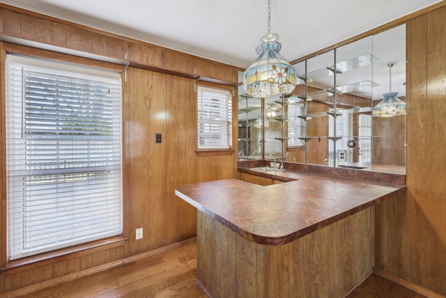 kitchen featuring kitchen peninsula, sink, pendant lighting, wood-type flooring, and wood walls