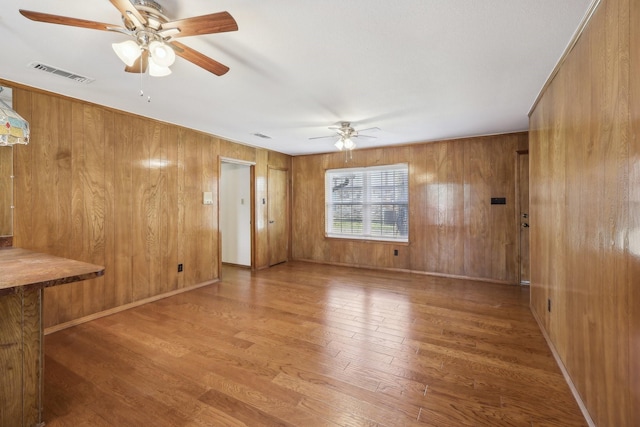 unfurnished living room featuring wood walls, hardwood / wood-style floors, and ceiling fan