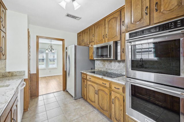 kitchen with light stone counters, a notable chandelier, backsplash, light tile patterned floors, and appliances with stainless steel finishes