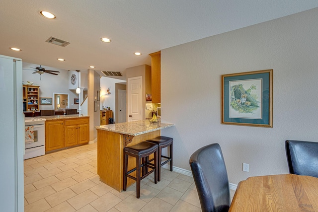 kitchen featuring a kitchen bar, electric range, ceiling fan, kitchen peninsula, and light stone countertops